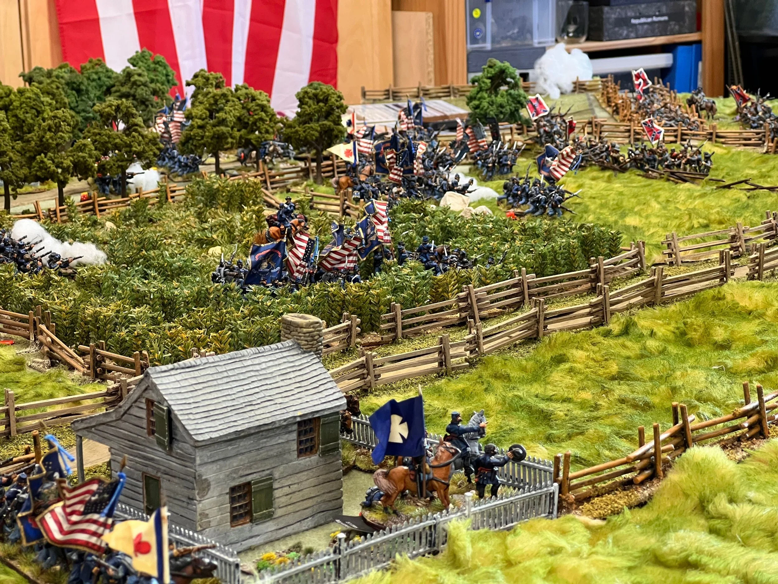 Miniature soldiers on a battlefield display with trees, fences, and a small house.
