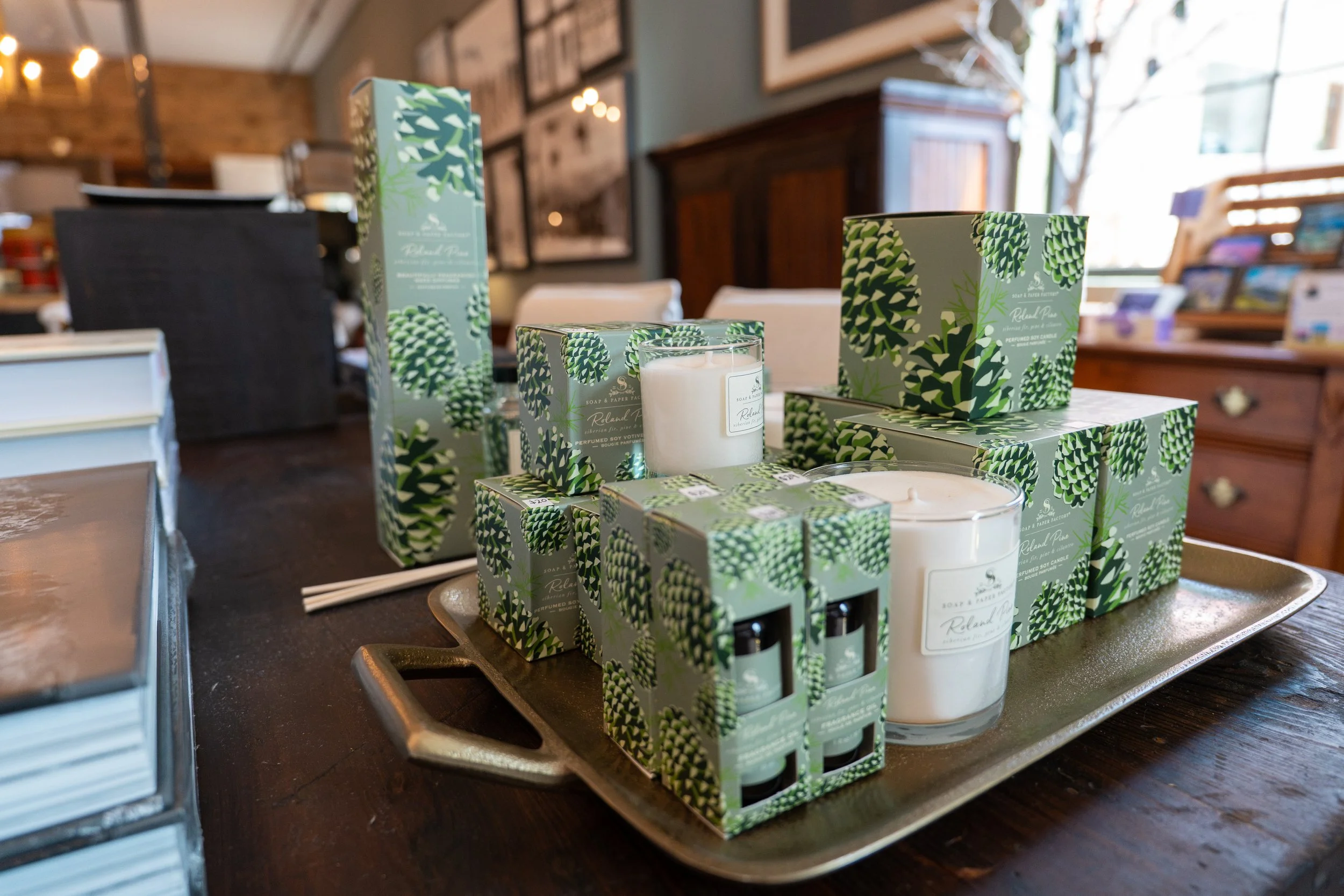 Display of scented candles and boxed soap products with green leaf and tree packaging design on a retail store table.
