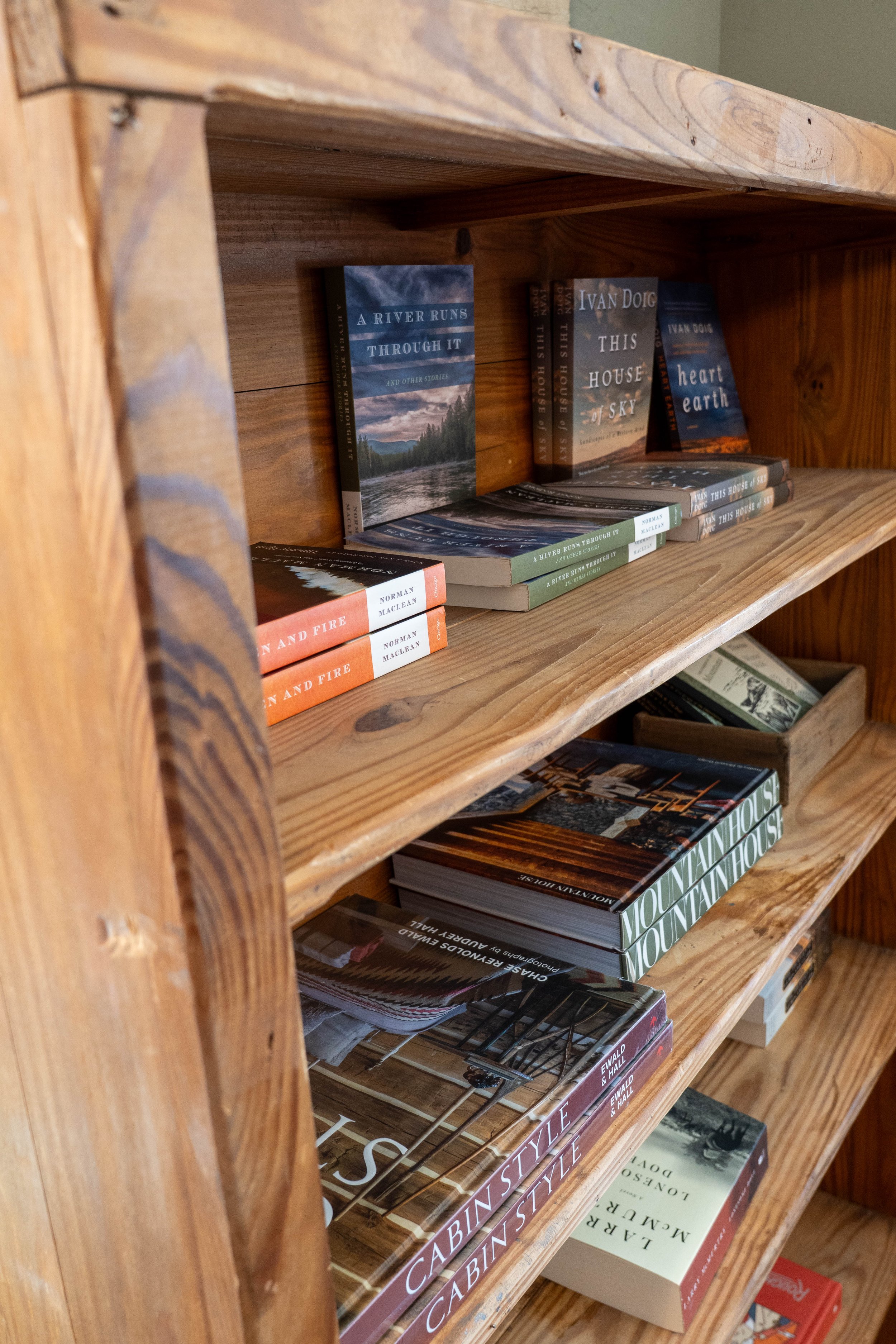 Wooden bookshelf with multiple books, including titles such as "A River Runs through It," "This House of Sky," and "Heart Earth."