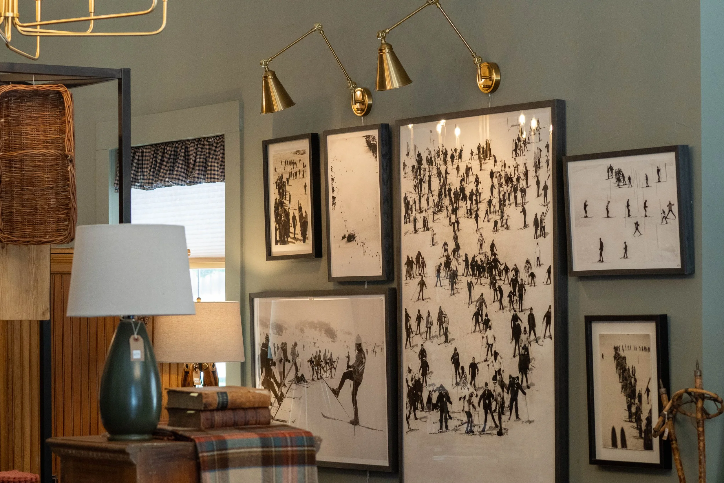 Interior of a room with framed black and white photographs of people, a table with books, and lamps with gold fixtures, with a window in the background.