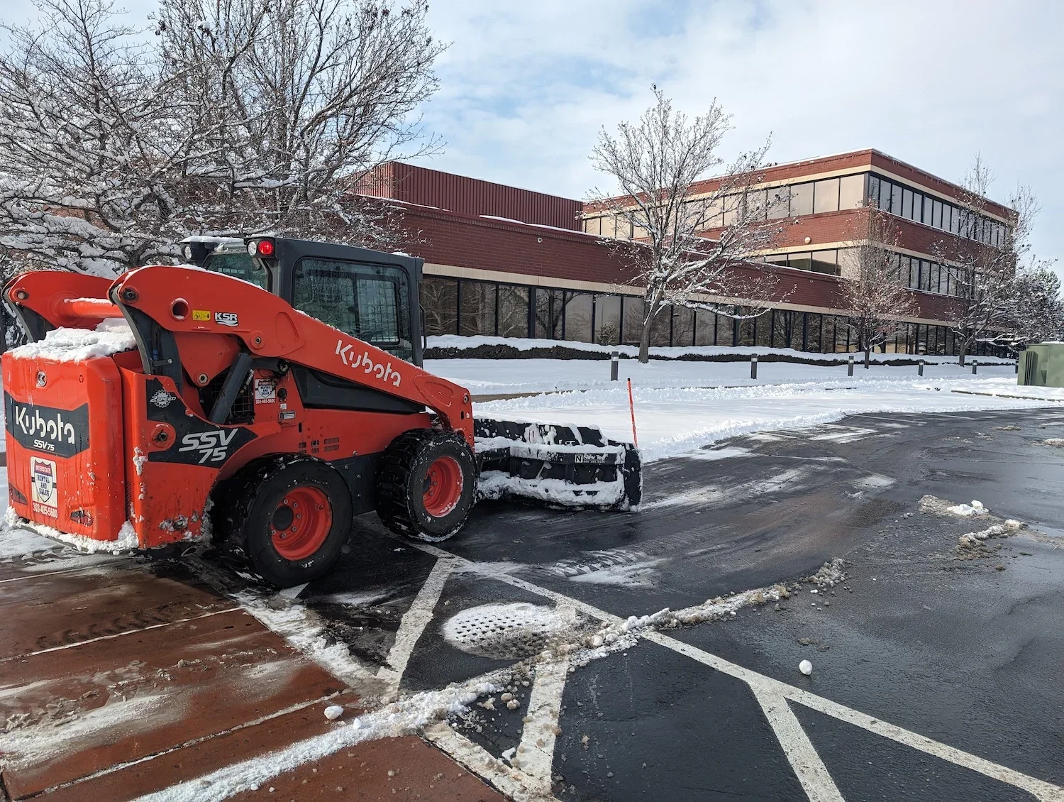red snow plow removing snow in front of commercial business.webp