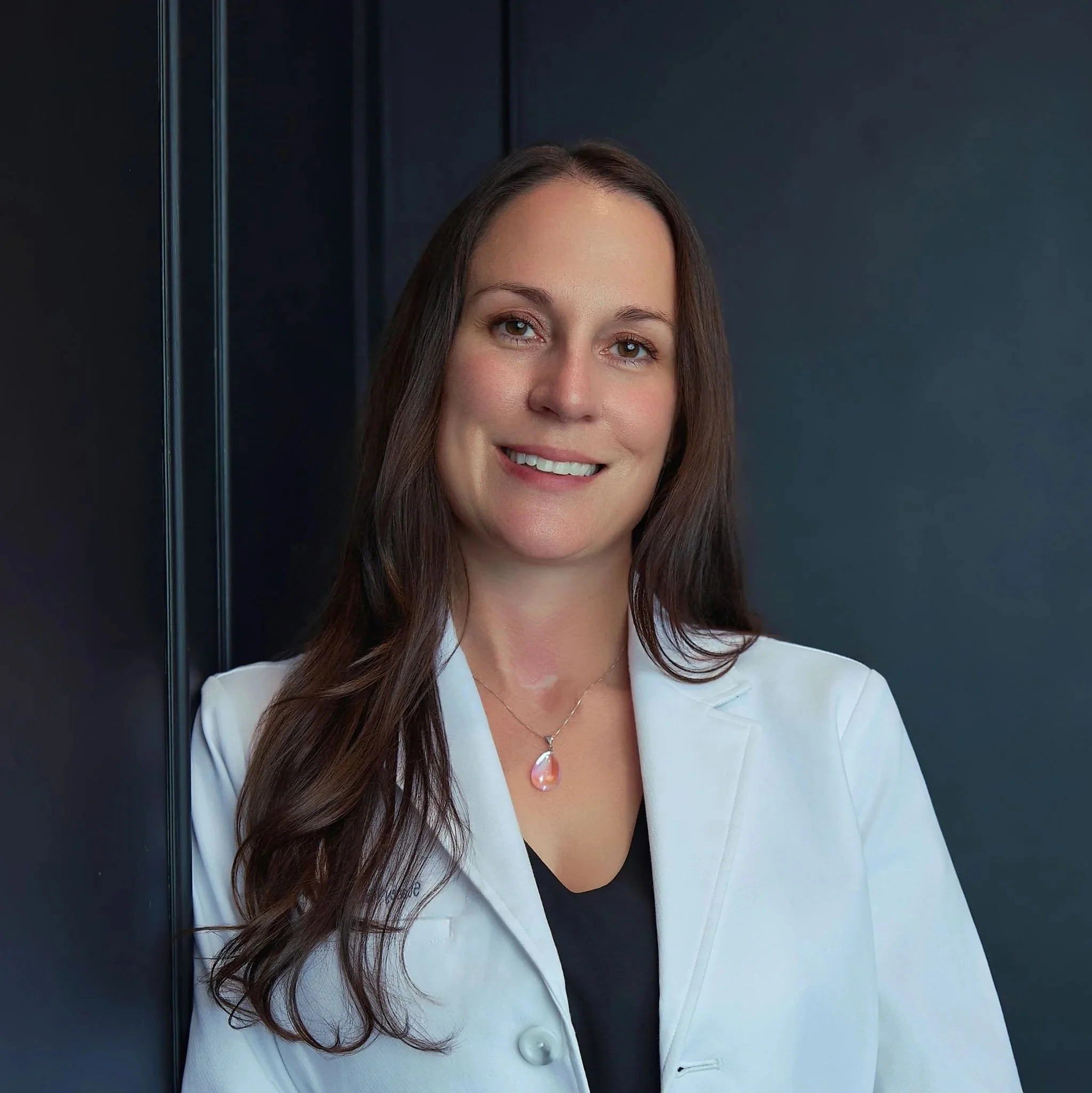 Close-up of Stacey Velimesis, PMHNP-BC, smiling, professionally dressed against a dark gray background.