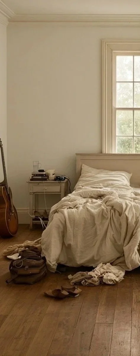 Untidy bedroom with unmade bed, clothes on the floor, a guitar, and a nightstand with miscellaneous items, before ADHD treatment.