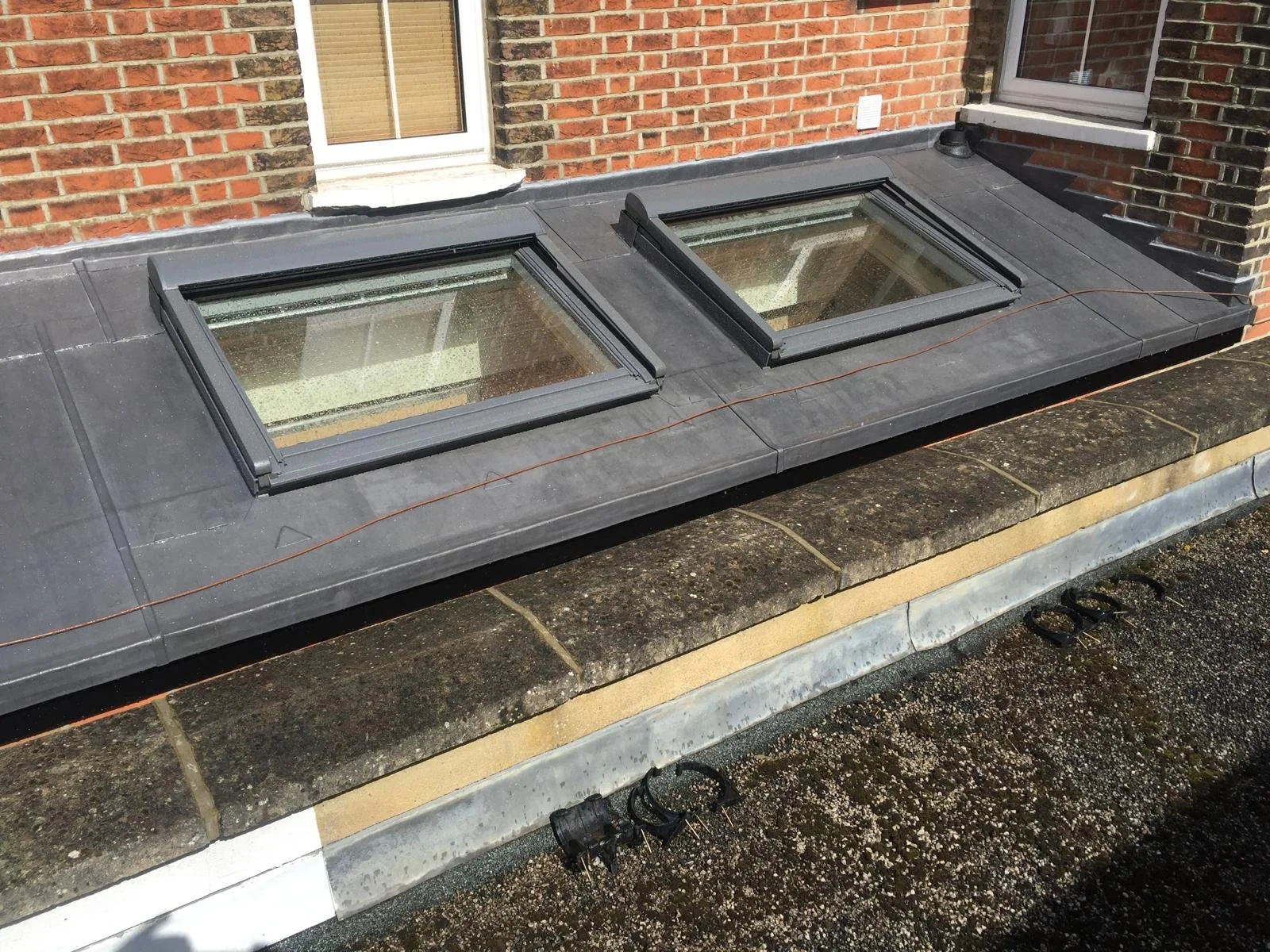 Roof with two skylights installed on a flat surface next to brick walls.