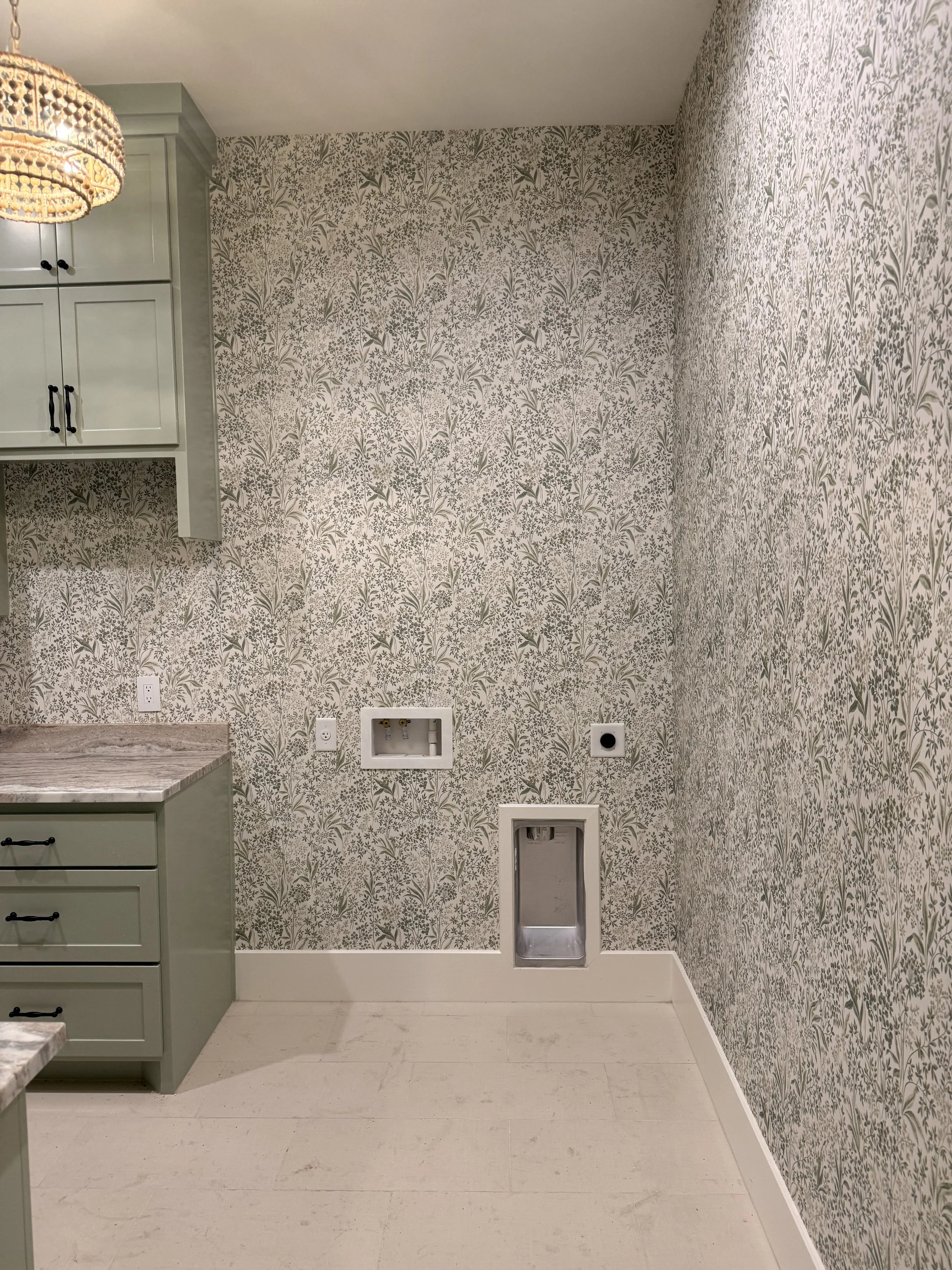 Empty laundry or utility room with floral-patterned wallpaper, a small mounted cabinet, and several connections for washer and dryer.