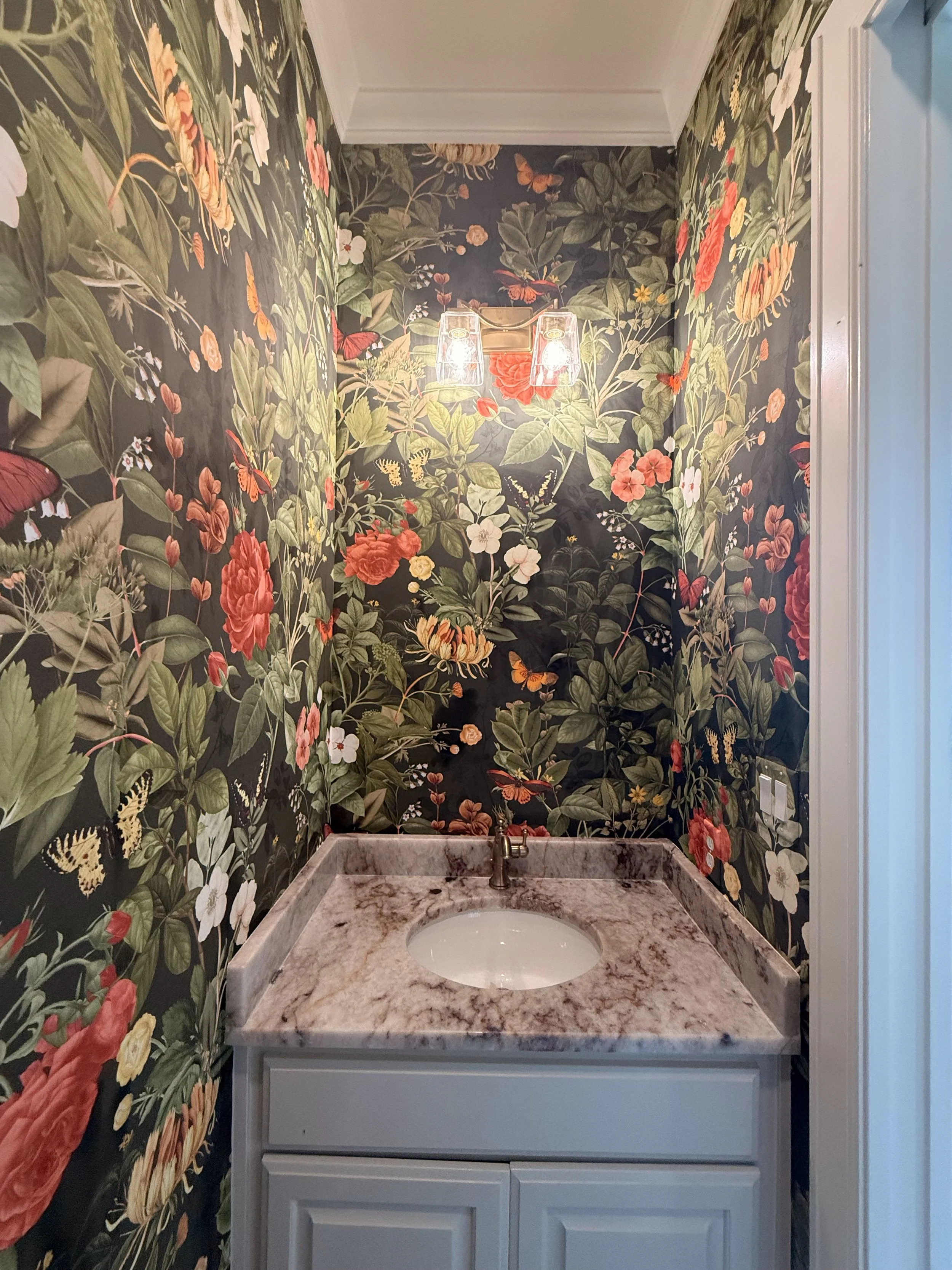 A bathroom vanity with a marble countertop and a white cabinet below, set against floral wallpaper with butterflies.