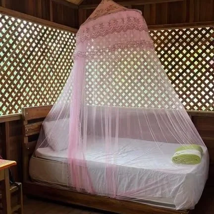 A bed with a pink canopy and mosquito netting in a wooden room with lattice walls, a folded green towel on the bed.