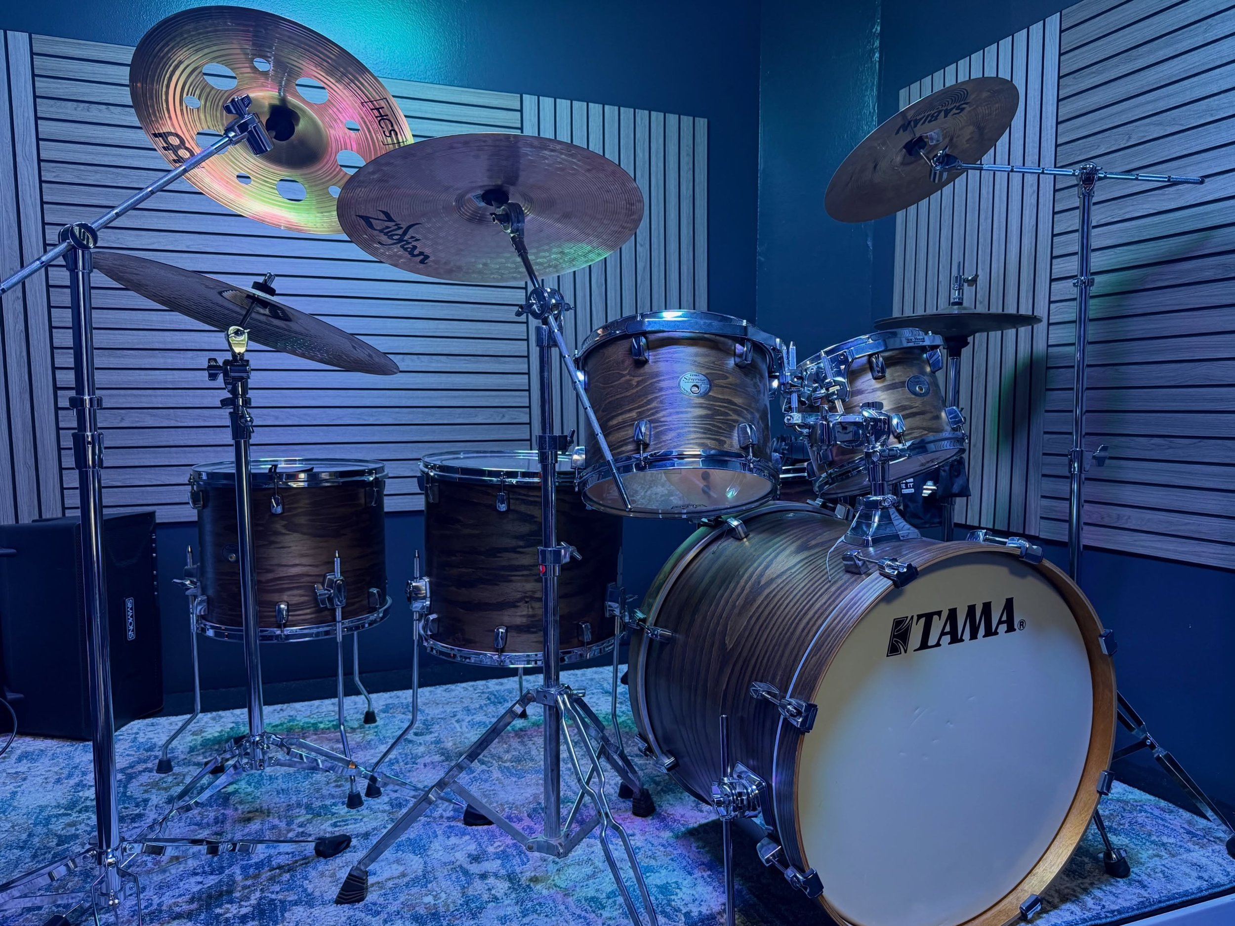 A Tama drum set with multiple drums and cymbals in a music studio, with soundproofing panels on the walls.
