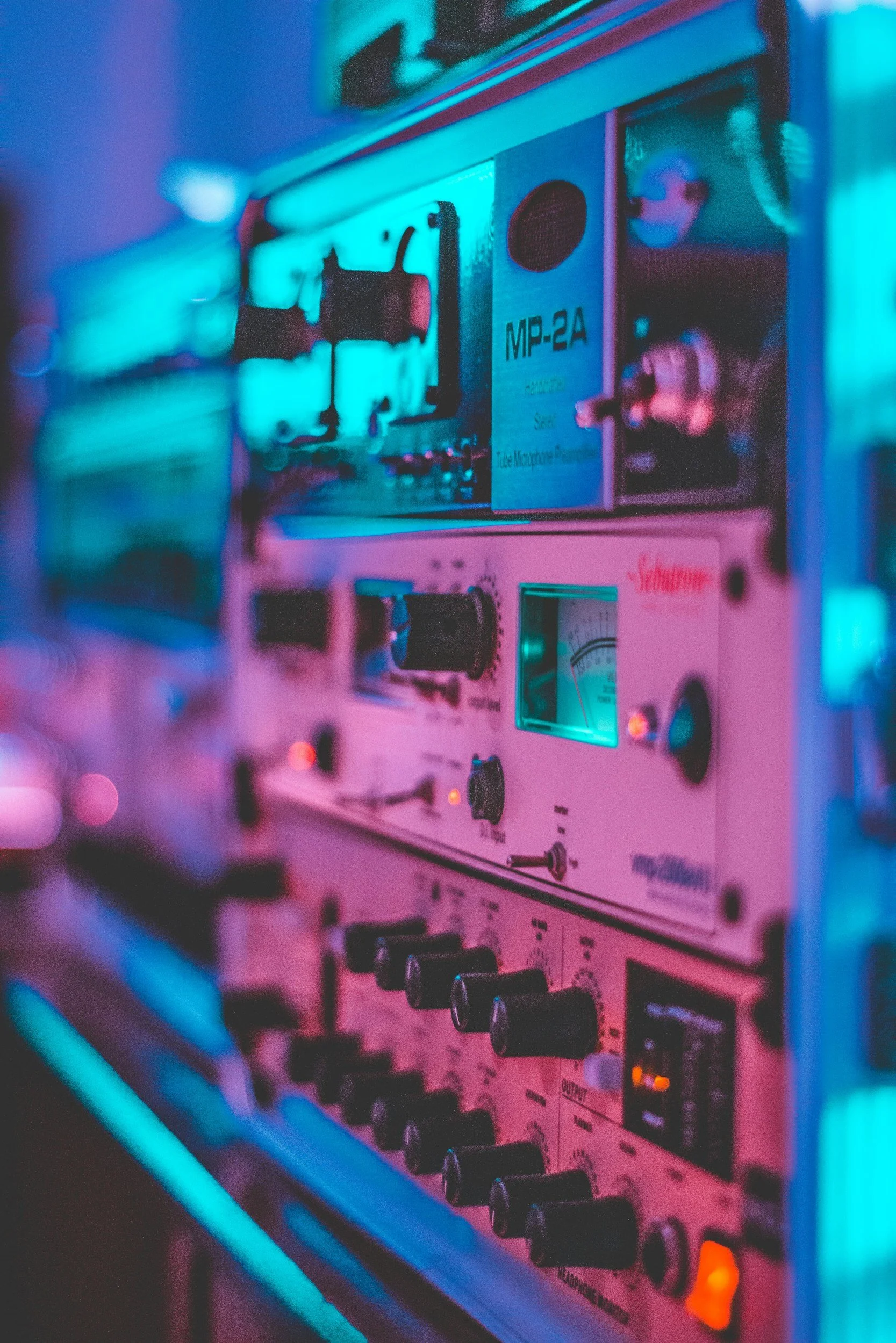 Close-up of an analog mixing console illuminated with blue and pink lighting, showing various knobs and controls.