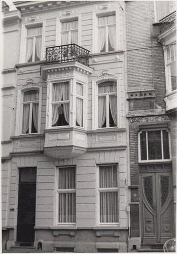 Historic European townhouse facade with ornate bay windows, wrought-iron balcony, tall sash windows, and decorative wooden entrance door