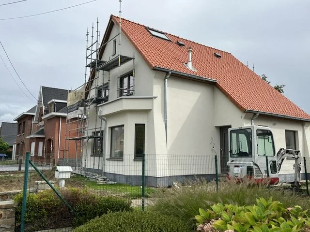 House under construction with scaffolding, red tile roof, and compact excavator in front
