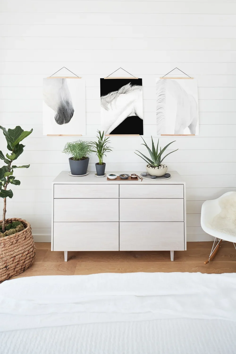 Bright minimalist bedroom with white dresser, potted plants, horse artwork, and a modern accent chair