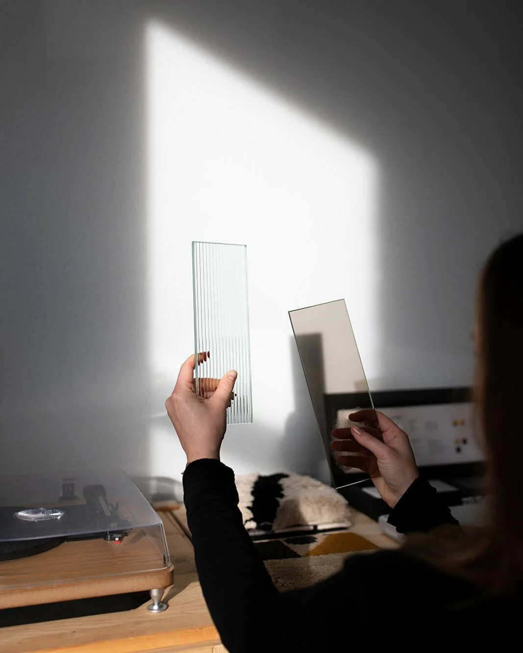 Person holding two samples of textured and tinted glass panels in a sunlit room