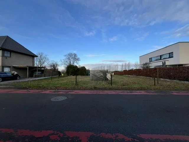 Vacant grassy lot between modern houses beside a residential street under a blue sky