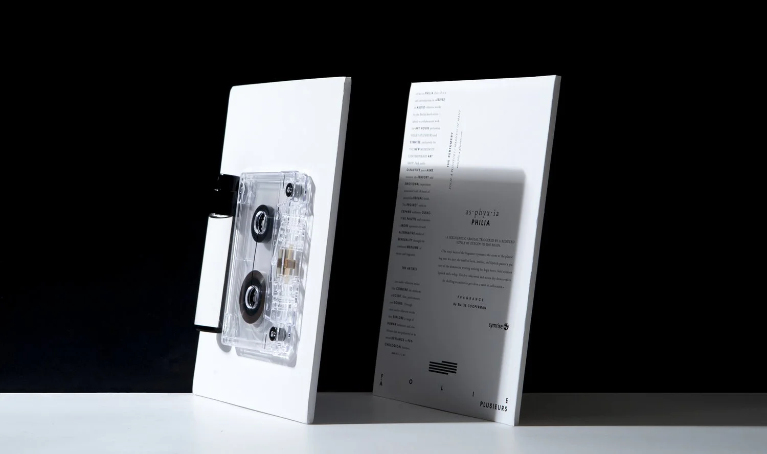 A white display board featuring a transparent audio cassette tape on the left and a white informational sheet on the right, against a black background.