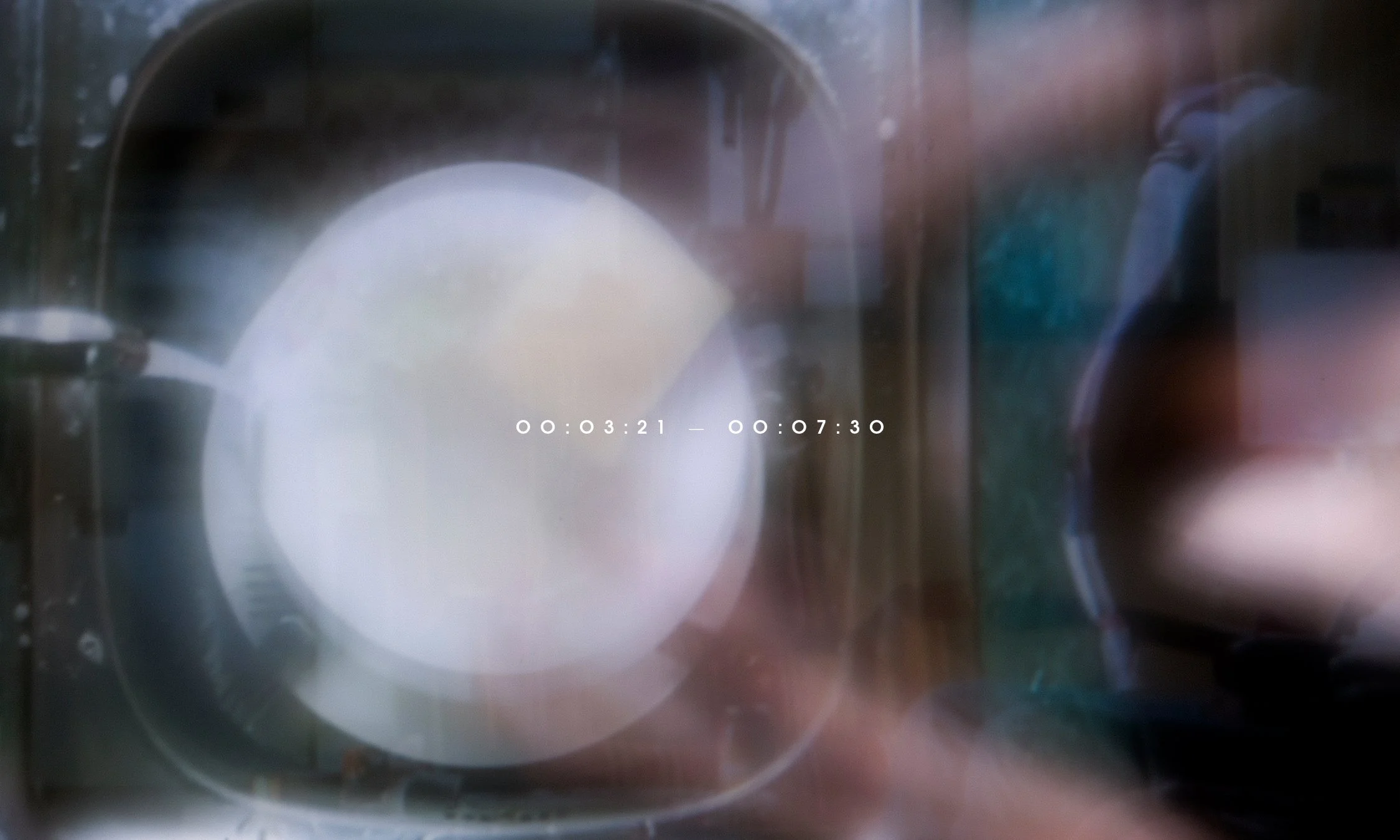A washing machine door with the drum visible, showing a puddle of water or some reflection inside, with timestamps overlaid in the center.