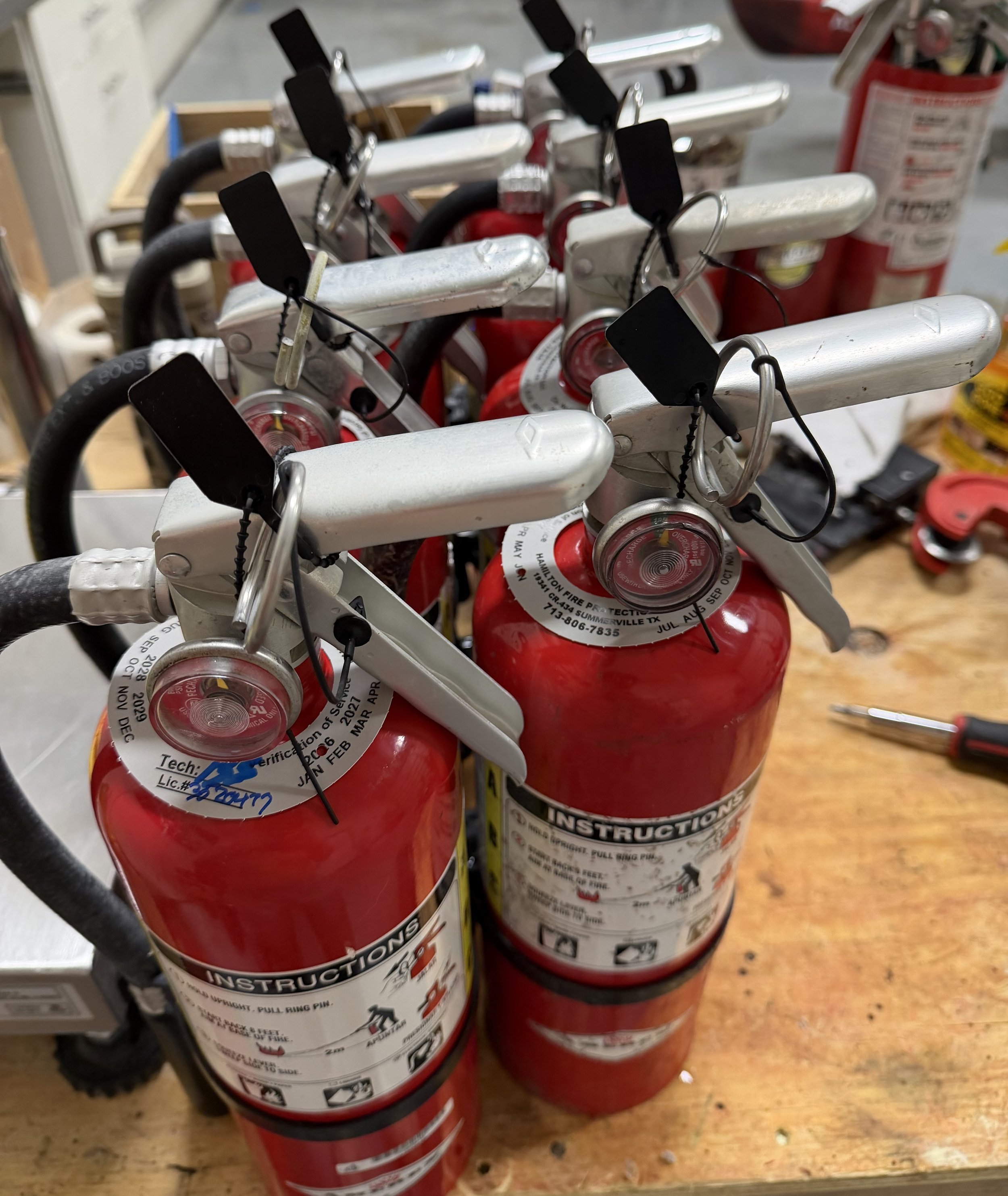 A group of red fire extinguishers with black tags hanging on top, placed on a wooden surface, with a fire extinguisher label visible.
