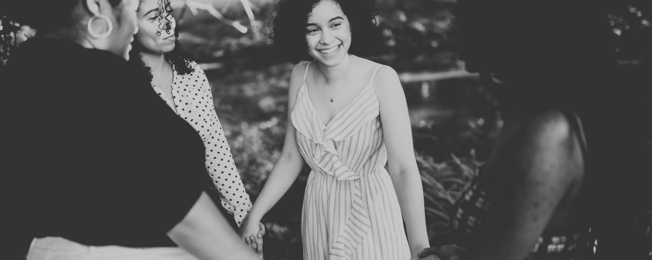 A group of four people holding hands in a circle outdoors, smiling and enjoying a moment of connection.