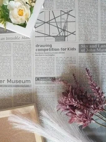 A flat lay of a newspaper with a flower arrangement and decorative branches on top.