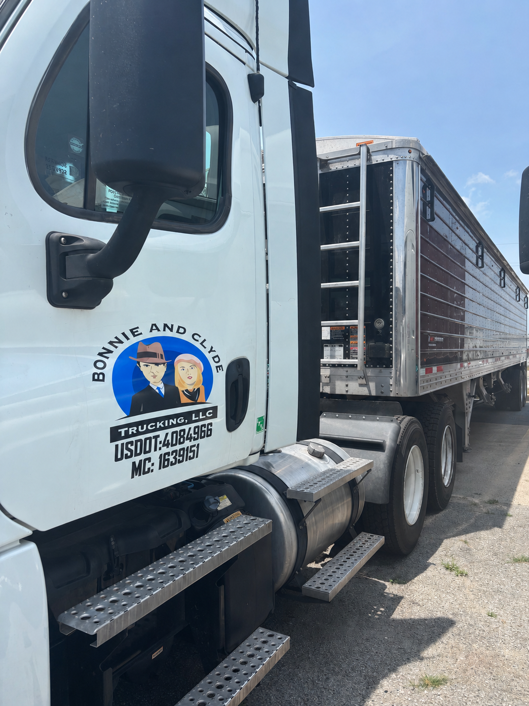 A white semi-truck with a black trailer parked on a paved road under a blue sky with some clouds. The truck has a logo for Bonnie and Clyde Trucking, LLC on the door.