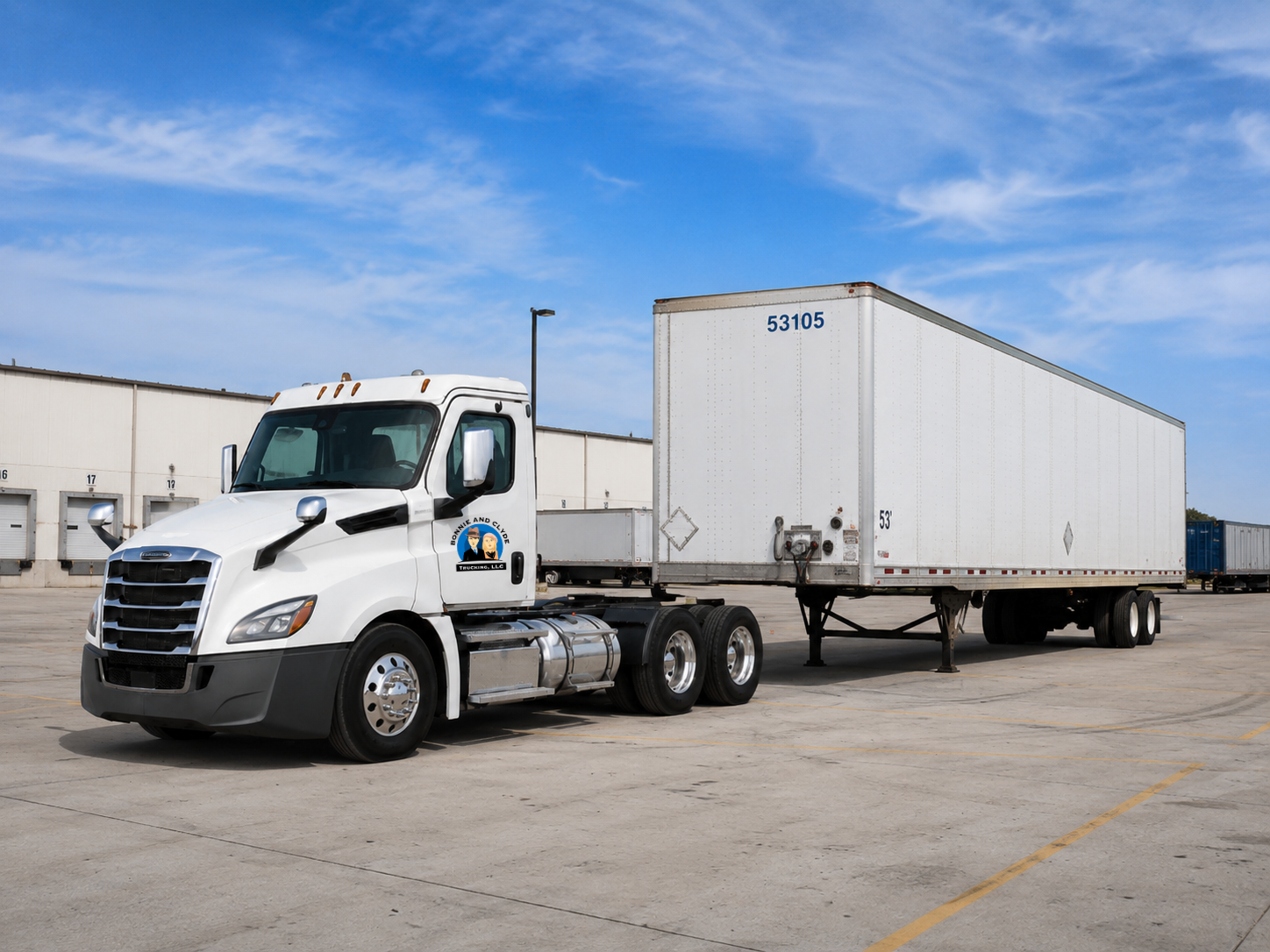 White semi-truck with a white trailer parked in a lot near a warehouse, under a partly cloudy sky.