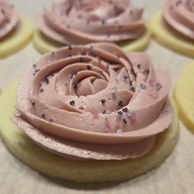 Round cookies topped with pink frosting piped in rose‑shaped swirls and sprinkled with purple and pink sugar crystals.