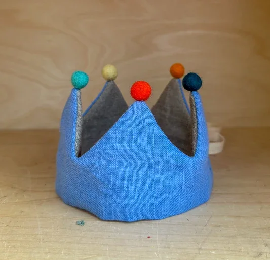 Handmade felt kids crown in blue fabric with colorful felt balls on each point, designed as a soft, child‑friendly accessory for birthdays, dress‑up, or imaginative play.