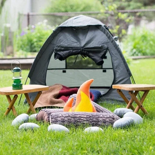 Handmade kids camping play set featuring a felt campfire with logs and stones, a small tent with blankets, and wooden tables with a lantern, arranged outdoors for imaginative play.