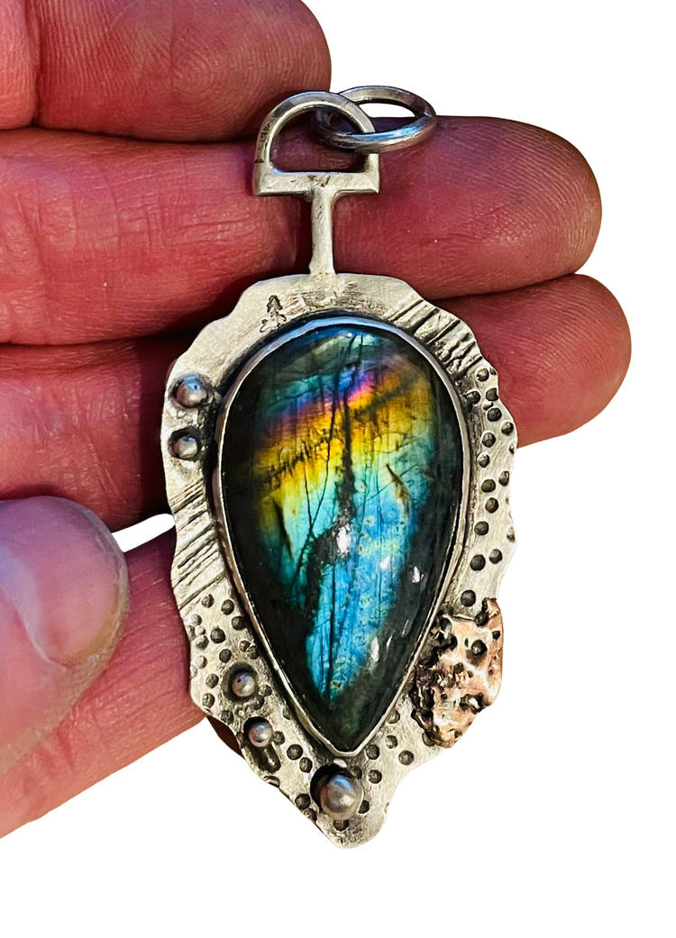 A handcrafted teardrop-shaped gemstone pendant with vivid iridescent colors, set in a textured silver frame with raised dot detailing and a T-shaped bail.