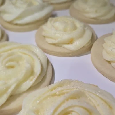 Round cookies topped with smooth white frosting piped in rose‑shaped swirls, arranged on a clean white surface.