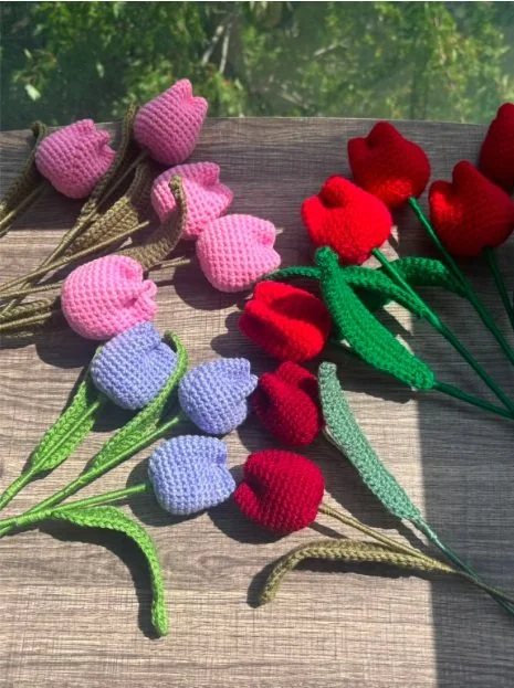 Handmade crochet tulip bouquet in pink, red, purple, and burgundy tones with green stems, crafted by Meraki The Soul Creativity and displayed on a wooden surface in natural light.