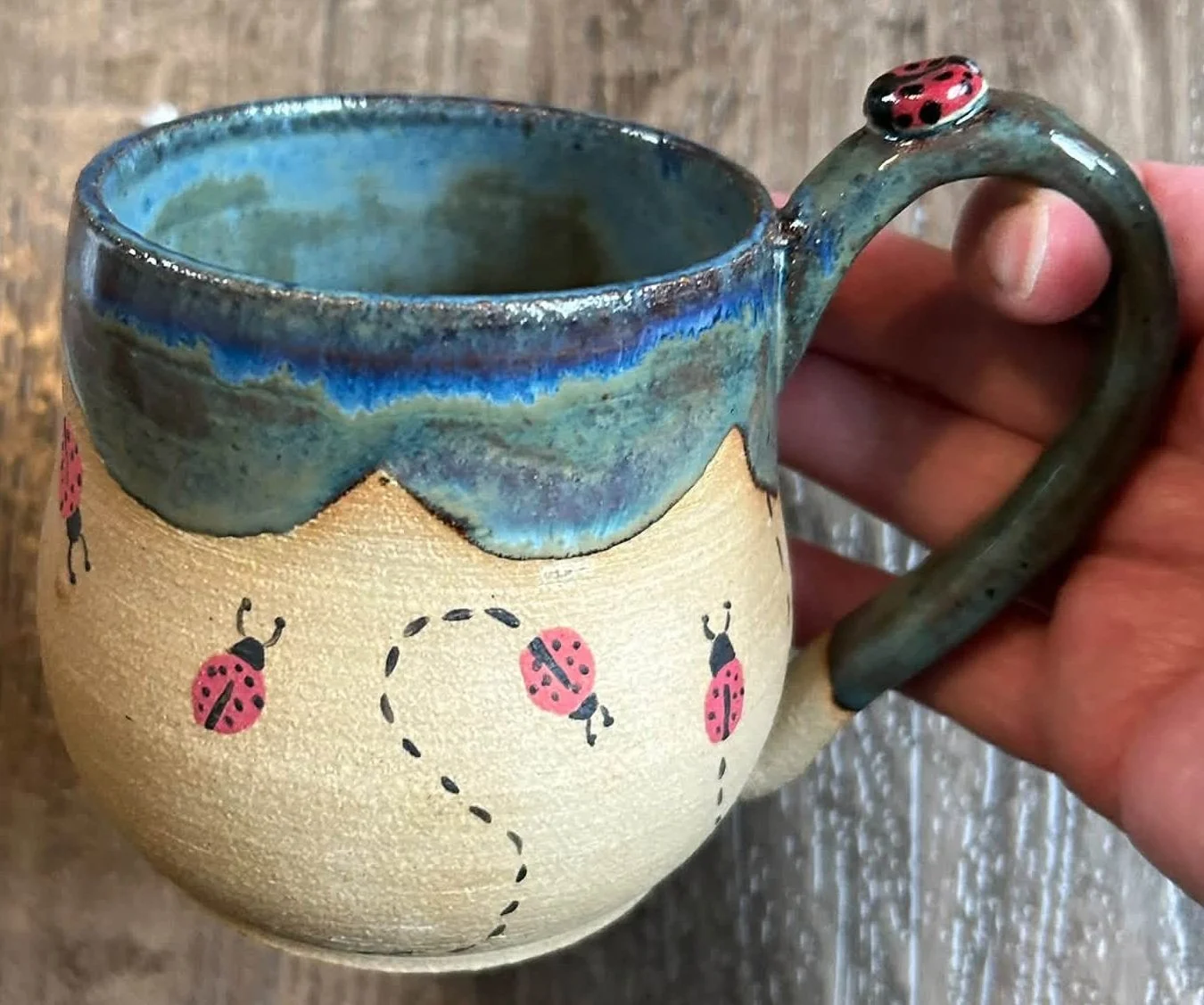 Handmade ceramic mug with blue-green glaze and textured ladybug design crafted by Purple Moon.