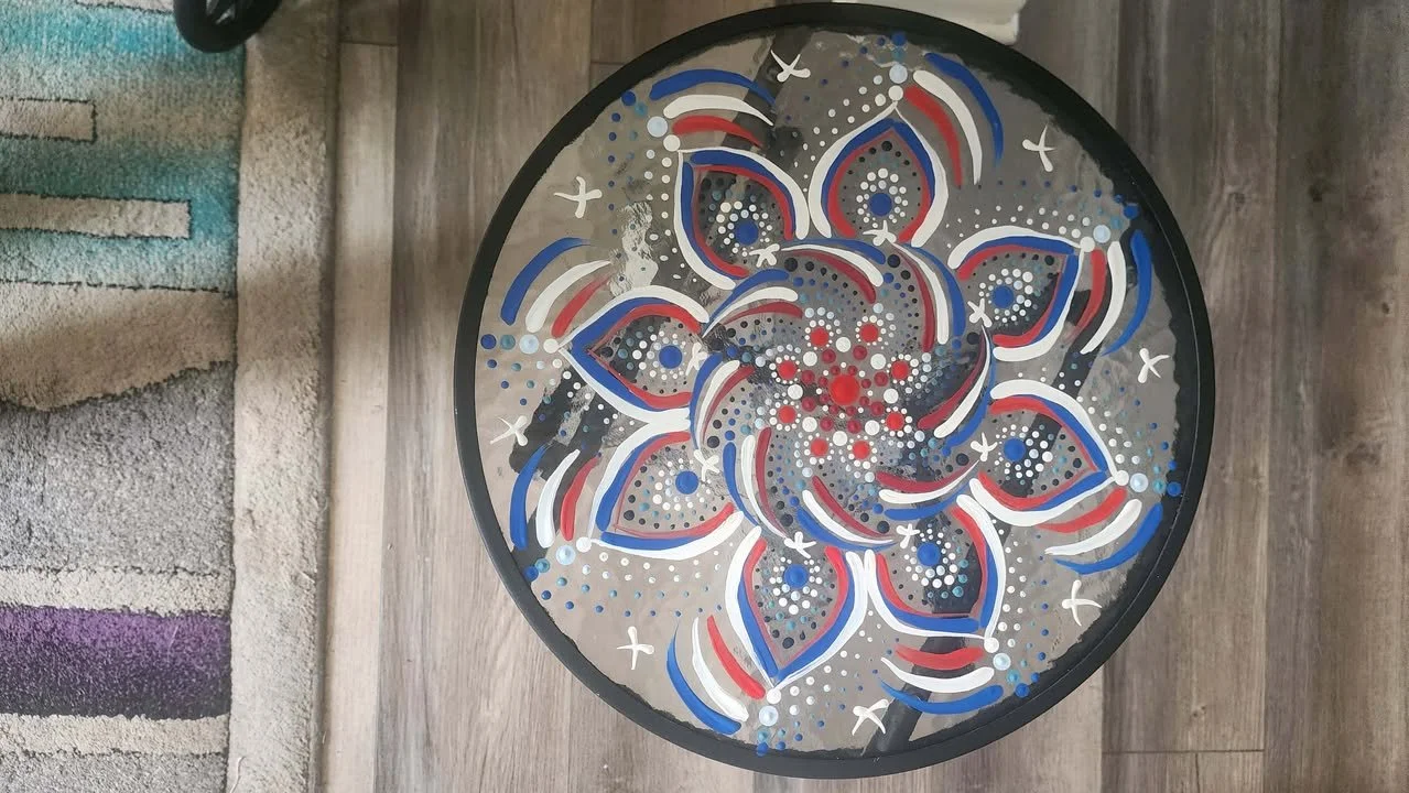 Circular tabletop decorated with a red, white, and blue spiral mandala pattern made with layered dot‑art details.
