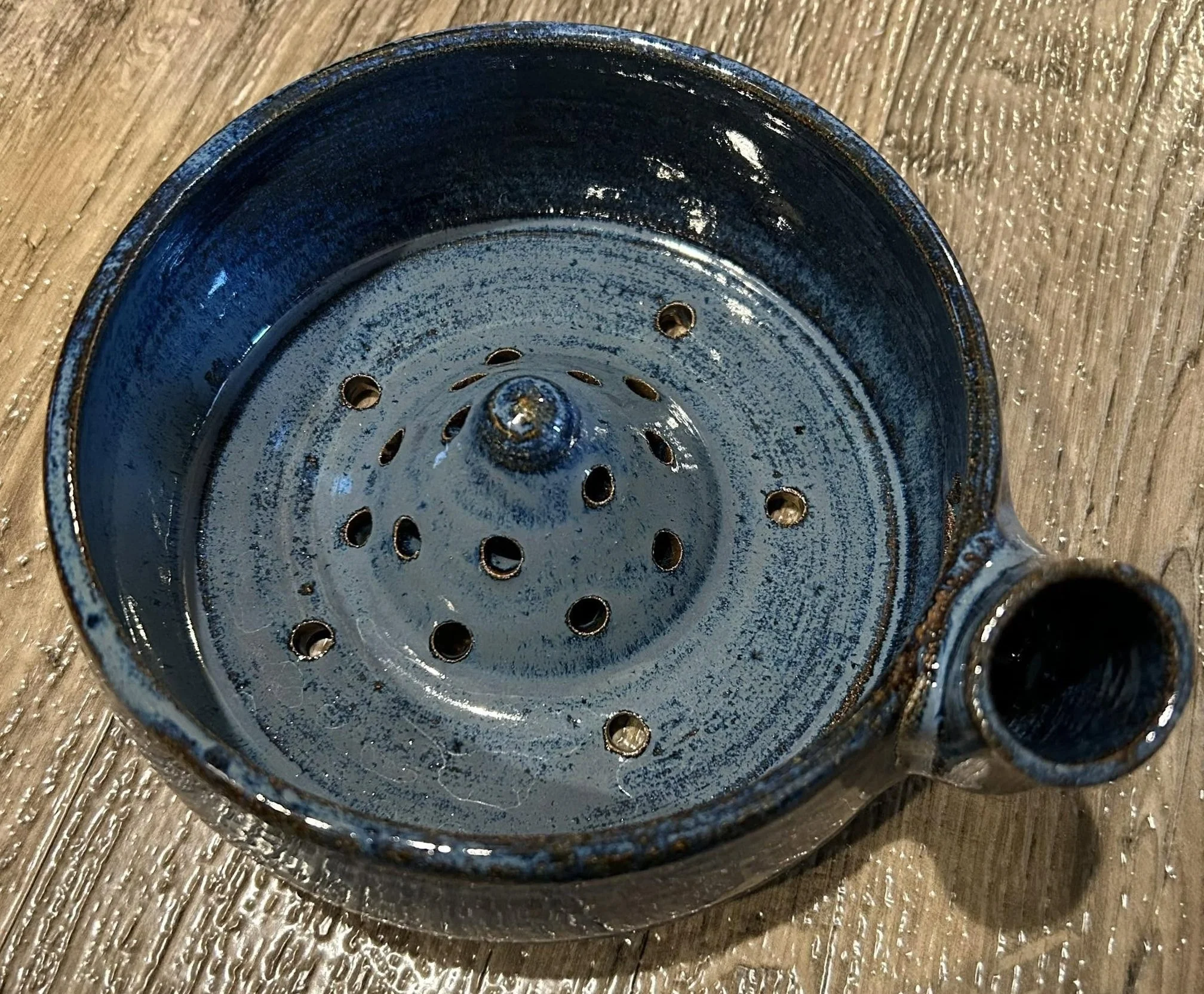 Handmade ceramic strainer with glossy blue glaze and raised perforated center crafted by Purple Moon.