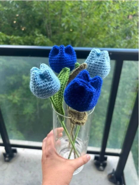 Handmade crochet tulips in light and dark blue shades arranged in a clear glass vase, crafted by Meraki The Soul Creativity and photographed outdoors in Waterloo, Iowa.
