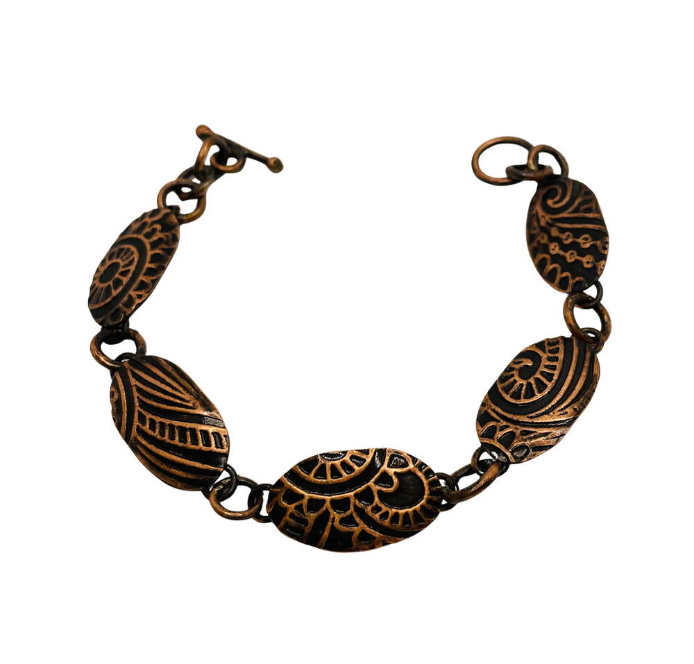 A handcrafted bracelet featuring engraved oval metal links connected by small rings, with intricate raised patterns and a toggle clasp.