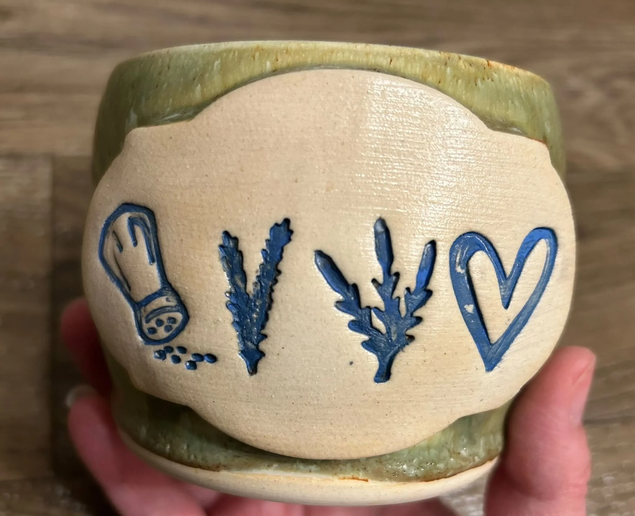 Handmade ceramic mug with green glaze and carved herb, salt shaker, and heart designs by Purple Moon.