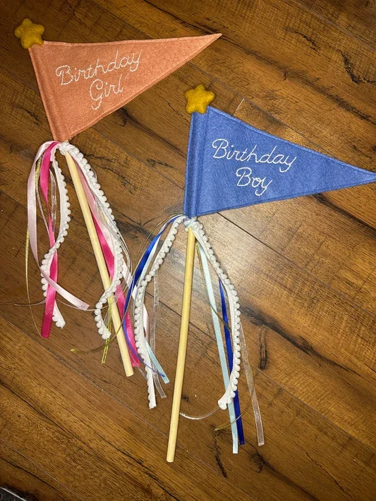 Handmade felt birthday wands with embroidered “Birthday Girl” and “Birthday Boy” flags, decorated with colorful ribbons, pom‑pom trim, and star accents.