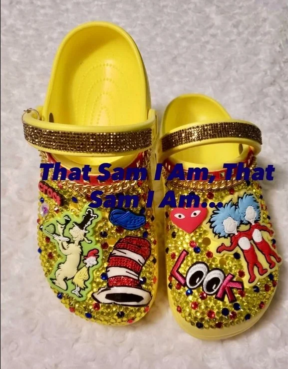 Custom yellow Crocs decorated with Dr. Seuss character charms, gold rhinestones, glitter straps, and colorful themed embellishments displayed on a white background.