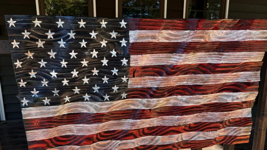 Handcrafted wooden American flag with carved wave texture, painted stars and stripes, and customizable patriotic design.