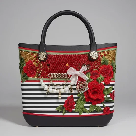 Hand‑embellished handbag with black handles, striped base, red rose embroidery, pearl accents, gold chains, and jeweled crown detailing.