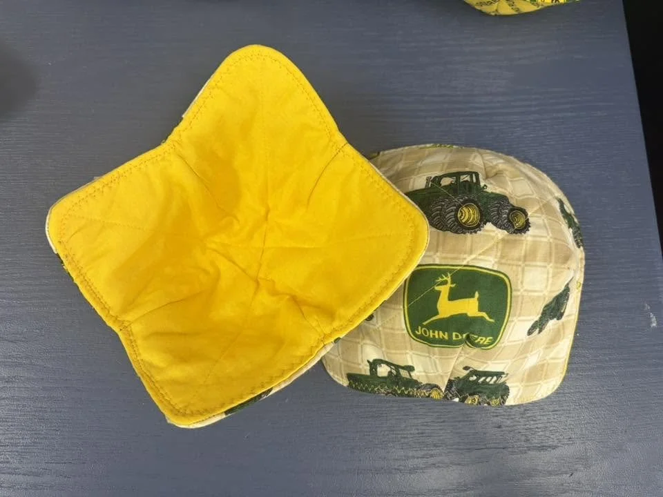 Handmade John Deere fabric bowl cozy with yellow quilted companion piece displayed on a dark surface.