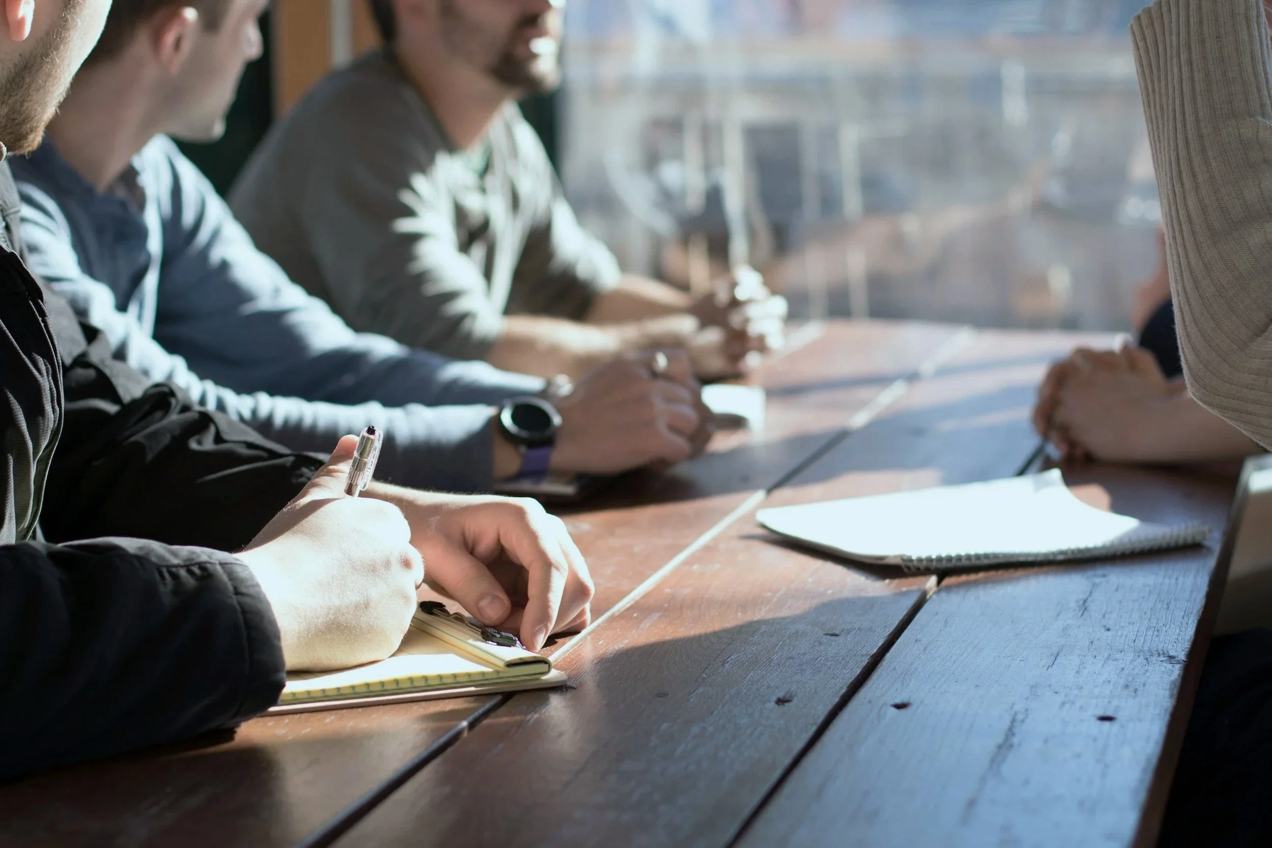 A 3 person sales team sitting at a table facing a sales coach, all with notepads and pens
