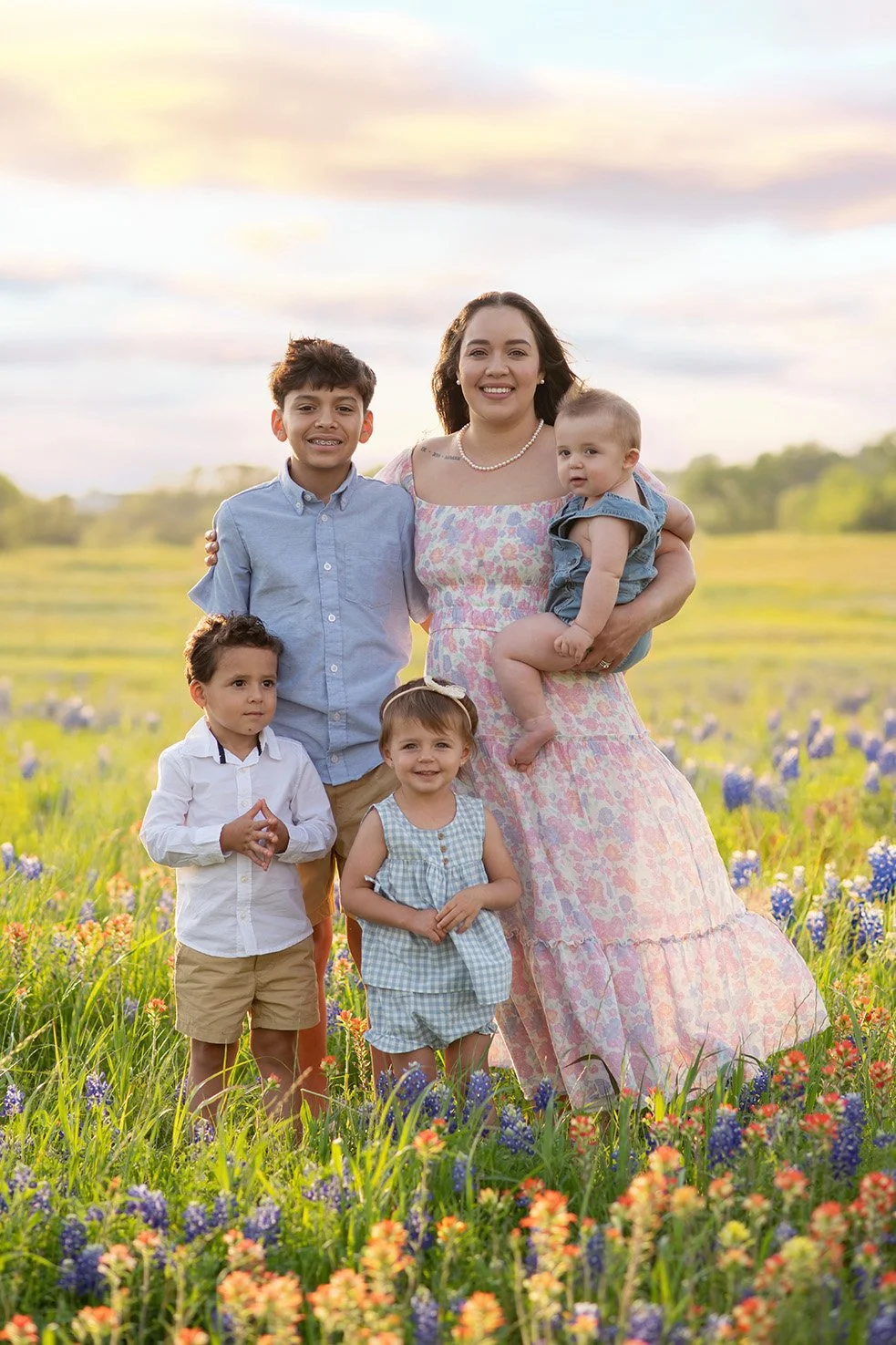 A woman with five children standing in a field of wildflowers during sunset, all smiling at the camera.
