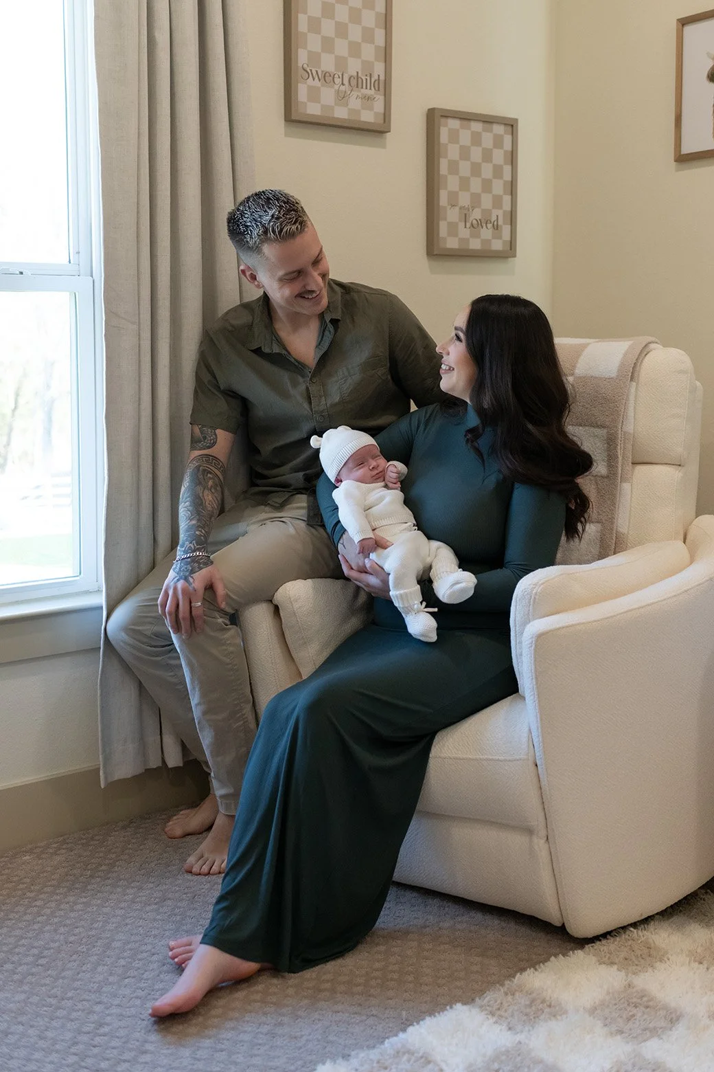 Family of three celebrating with a newborn baby in a cozy living room, woman holding the baby, man sitting beside her, all smiling.