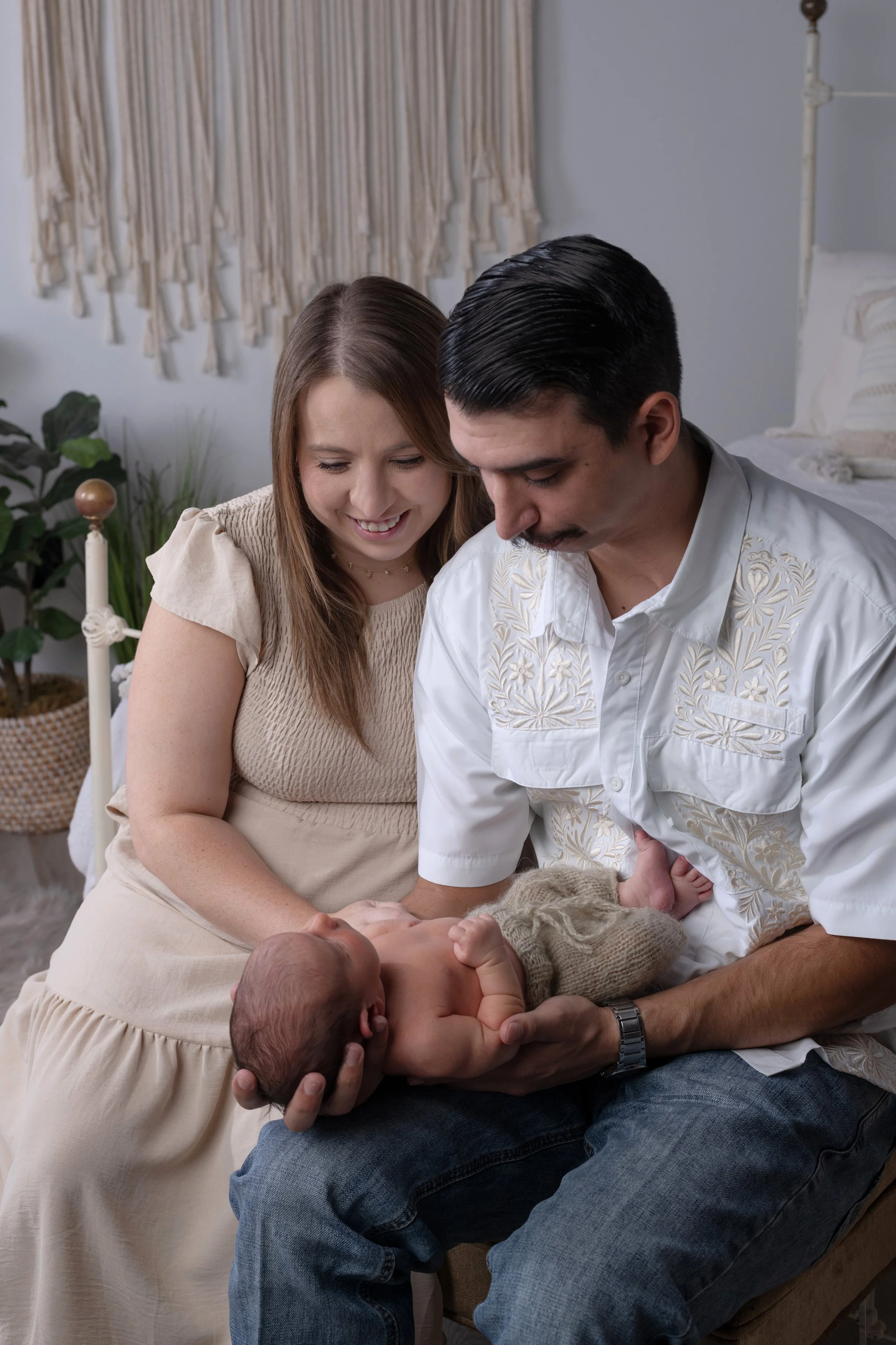 A couple surrounded by family members holding a newborn baby in a cozy home setting.