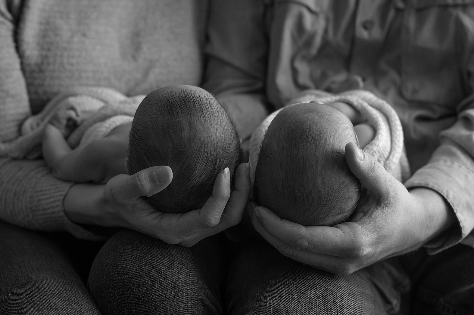 Two infants with bald heads, cradled in the hands of an adult. The photo is in black and white.