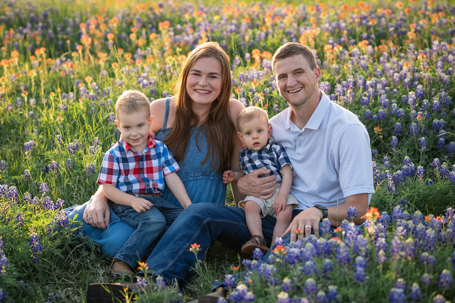 A family of four sitting in a field of purple and orange wildflowers, smiling at the camera during daylight.