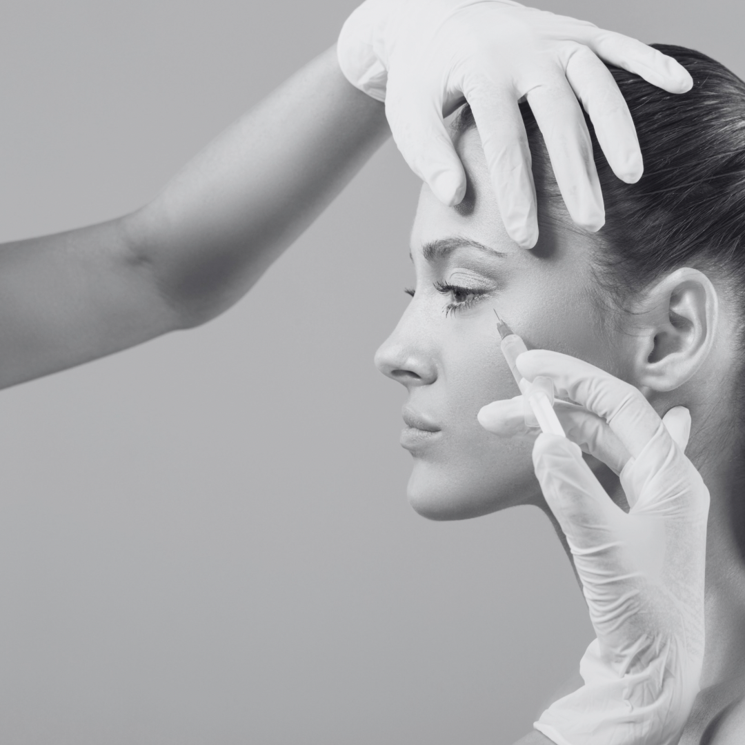 A woman receiving a cosmetic injection near her eye from a healthcare professional wearing gloves.