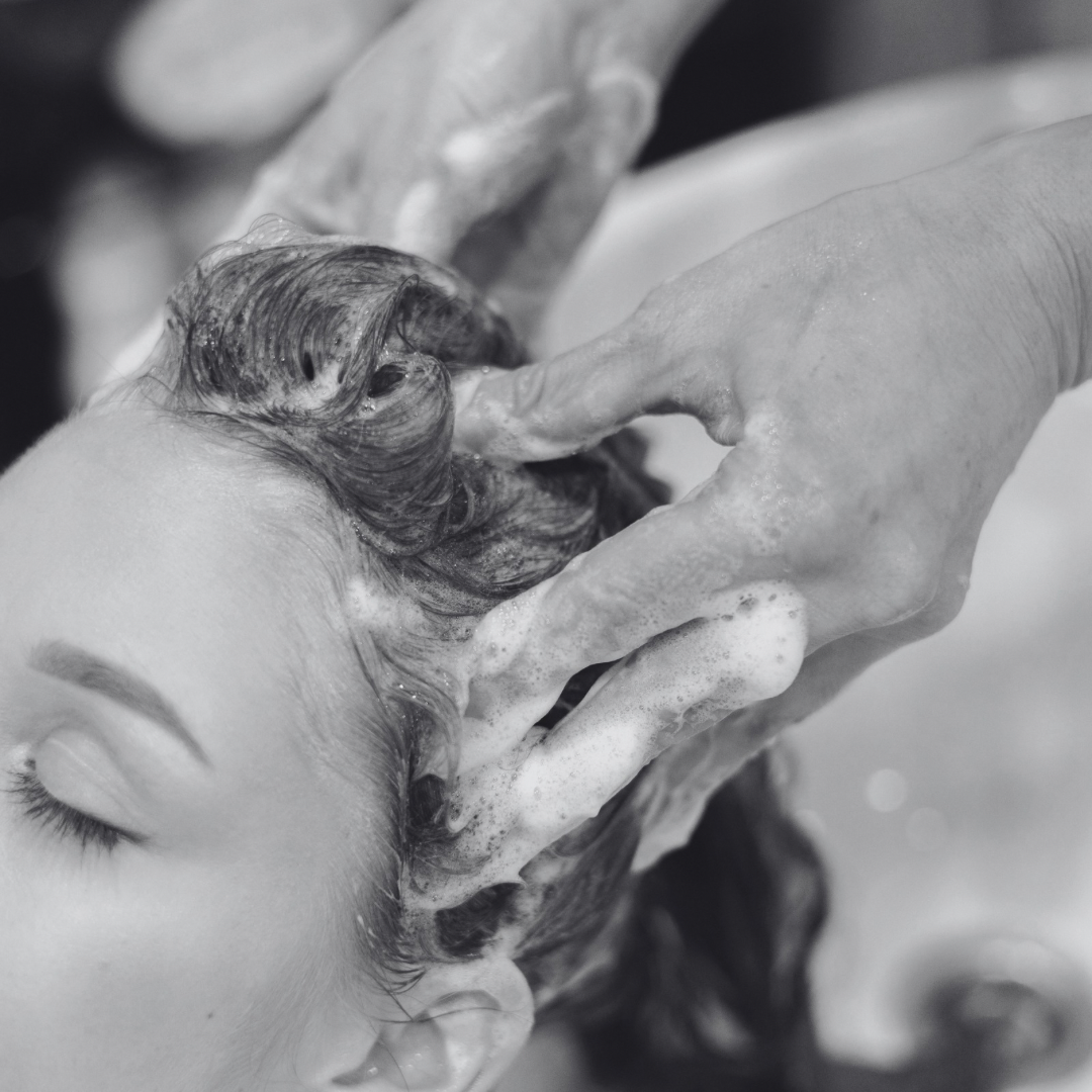 A woman with closed eyes washing her hair with soap lather in a shower.